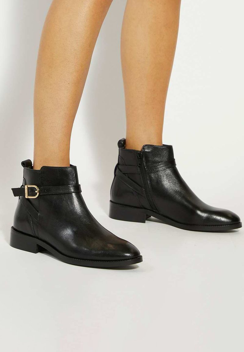 Black ankle boots made of smooth leather, featuring a side zipper, adjustable strap with a gold buckle, and a low, block heel.
