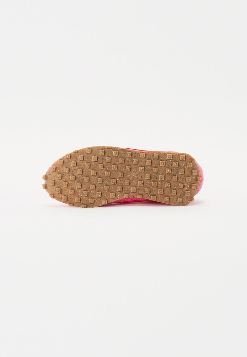 Zapatilla deportiva rosa con una suela de goma texturada que presenta patrones cuadrados y hexagonales, diseñada para proporcionar agarre y tracción.