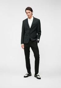 Svart skräddarsydd kostym med en knapp, vit skjorta och svarta byxor. Svart och vit tvåtonsskor avslutar outfiten.