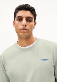 Lichtgroen katoenen t-shirt met een ronde halslijn en een blauw "ARMEDANGELS" logo, met korte mouwen en een gladde textuur.