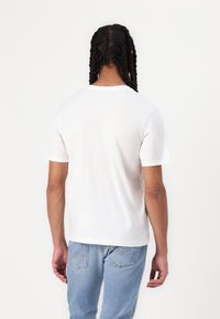 Hvid bomulds t-shirt med korte ærmer, rund halsudskæring og en glat tekstur, båret med lyseblå denim jeans. Bagfra billede af tøjet.