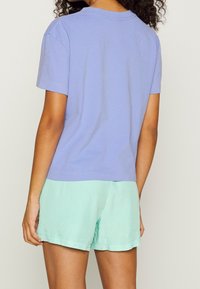 Camiseta de manga corta en lavanda con cuello redondo, combinada con pantalones cortos en verde menta. Ambos están confeccionados con tela suave y presentan colores sólidos y simples.