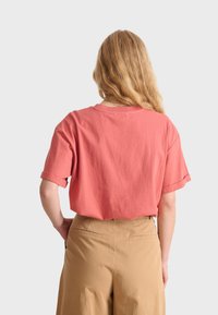 Kortärmad t-shirt i korallrosa med en avslappnad passform och upprullade ärmar, tillverkad av mjukt bomull. Bärs med beiga högmidjade byxor.