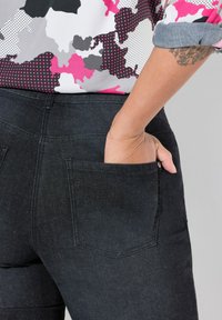 Pantalons en denim noir avec une taille mi-haute, dotés d'une poche à l'arrière et d'une texture lisse, associés à une chemise à motifs colorés.
