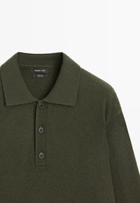 Oliwkowa wełniana koszulka polo z żebrowanym kołnierzykiem, trzema czarnymi guzikami i teksturowanym wzorem dzianiny. Metka marki widoczna wewnątrz kołnierzyka.