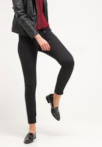 Svarta smala jeans i stretchy tyg med en slät yta, med en midja i medelhöjd och ankel-lång skärning. Matchas med glänsande svarta skor.