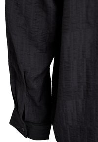 Melna krekls ar teksturētu audumu un vertikālām svītrām. Apkakle ar pogām un vaļīga piegriezuma dizains. Nav redzamu raksta detaļu.