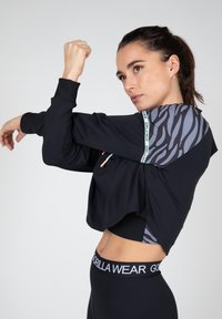 Zwarte cropped sweatshirt met een gestructureerde grijs- en zwart-gepatenteerde schouder, voorzien van een logoband langs de naad en aansluitende zwarte legging.