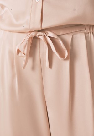 Blouse rose clair avec une texture lisse et soyeuse, dotée d'une taille nouée et de petits embellissements décoratifs.