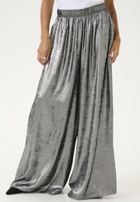 Pantalons larges en argent métallique avec une surface lisse et légèrement texturée. Dotés d'une ceinture élastique pour le confort et d'un design fluide.