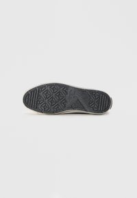 Suela de zapato de goma negra con un patrón texturizado y formas de estrellas para mayor agarre, con un borde beige. Superficie suave con un diseño robusto.