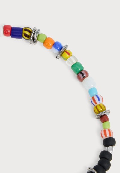 Brin incurvé de perles rondes colorées avec motifs mélangés et perles intercalaires argentées sur fond gris clair.