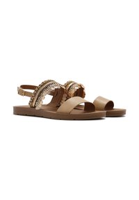 Tan flat sandals with open toe and ankle strap. Decorative bands feature rows of metallic coins and braided accents. Smooth texture.