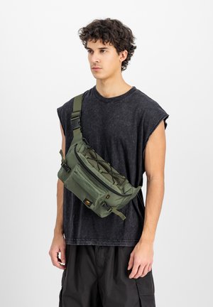Green crossbody bag with multiple zippered compartments, textured straps, and a front mesh overlay. Worn by a male figure in casual attire.