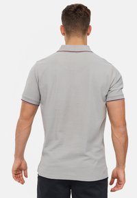 Šedé polo tričko s žebrovaným límečkem, krátkými rukávy a vínovými akcenty. Hladká látka a těsně padnoucí design, zobrazení zadního pohledu.