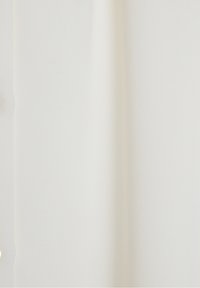 Tissu blanc drapé en douceur, présentant une texture douce avec un léger éclat. Une rangée de petits boutons court verticalement sur un côté.