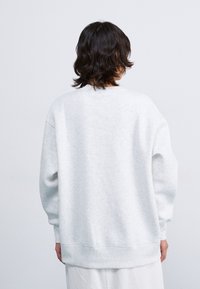 Sweatshirt oversize gris clair avec un col rond, des poignets et un ourlet côtelés. Fabriqué en tissu doux et texturé. Design épuré et minimaliste.