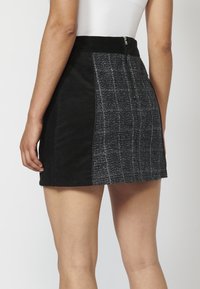 Jupe en denim noir avec un panneau latéral texturé et à motifs. Fermeture éclair à l'arrière, avec une coupe ajustée et une longueur mi-cuisse.
