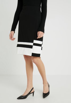 Schwarzer figurbetonter Rock mit weißen und schwarzen Streifen am Saum. Glatter Stoff, knielang, Seitenschlitz-Detail, kombiniert mit schwarzen Slingback-Absätzen.