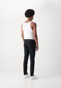 Zwarte slim-fit broek met een gladde textuur, standaard zakken en een discret label op de achterkant, gecombineerd met een witte tanktop.