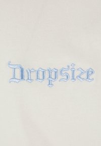 Hvidt stof med blå broderet tekst "Dropsize" i en stiliseret skrifttype. Teksturen er glat og let struktureret på grund af broderiet.