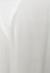 Vitt tyg med en slät textur och ett subtilt, kviltat mönster. Materialet verkar lätt och flytande, med en mjuk lyster.