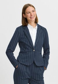 Námořnický blazer s jemným proužkem, s jednořadým zapínáním na knoflík, s klopami a dvěma předními kapsami. Vyroben z hladkého materiálu s přiléhavým střihem.