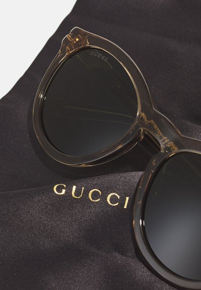 Gucci prillid selge, ülisuure, kassi silma raami, tumedate läätsede ja kuldse logoga mustal satiinist kotil.