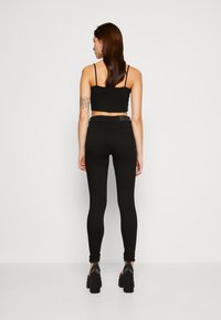 Top corto negro combinado con jeans ajustados negros. El conjunto presenta un ajuste ceñido, textura suave y diseño de cintura alta, llevado con tacones gruesos.