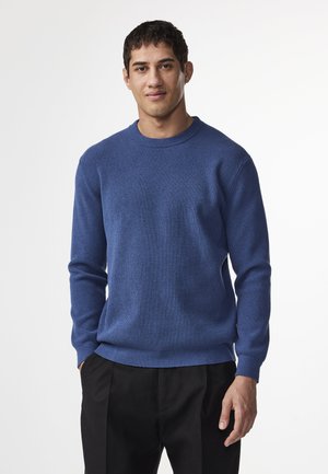 Pull en bleu à col rond avec une texture côtelée, des manches longues et une coupe décontractée, associé à un pantalon noir. Design simple et polyvalent.
