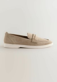 Mocassin beige en daim à enfiler avec semelle en caoutchouc blanche, bout arrondi et lanière décorative sur le dessus.