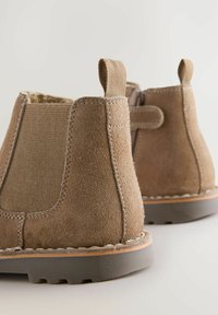 Bottines en suède marron avec des panneaux latéraux en élasthanne, des languettes de tirage et une semelle en caoutchouc. Les détails de couture améliorent le design global.