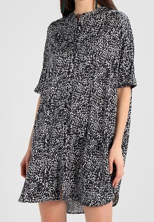 Robe ample à manches courtes noire et blanche à motifs, avec détail de boutons sur le devant et une légère fente avant, portée mi-cuisse.