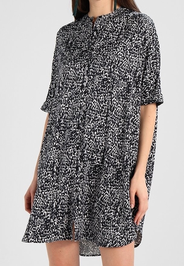 Robe ample à manches courtes noire et blanche à motifs, avec détail de boutons sur le devant et une légère fente avant, portée mi-cuisse.