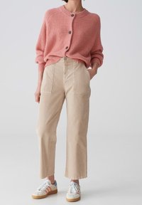 Cardigan tricoté rose clair avec boutons, associé à un pantalon beige taille haute à jambes larges et des baskets multicolores à lacets.