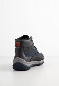 Zapato de senderismo de media altura en cuero azul marino y negro, con lados texturizados, acento rojo y suela de goma gris. Presenta detalles de cordones para mayor soporte.