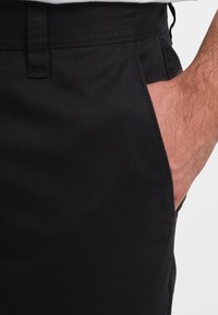 Pantaloni in cotone neri caratterizzati da una texture liscia, design classico, dettagli con tasche laterali e taglio dritto.
