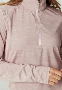 Lyserød atletisk pullover med lynlås ved halsen, der har et tekstureret mønster og lange ærmer med tommelfingerhuller for ekstra dækning.