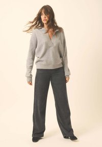 Grauer Wollpullover mit V-Ausschnitt und lockerer Passform, kombiniert mit dunkelgrauen weiten Jeans. Weiche Textur und entspannte Silhouette.