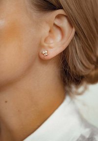 Boucles d'oreilles en or avec deux petites perles et un groupe de trois pierres scintillantes, ornées d'un délicat design floral.