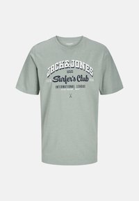 Light green cotton t-shirt with short sleeves and crew neck. Features navy blue text: "JACK & JONES Surfer's Club" and additional details below.