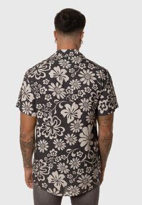Camisa de manga corta con cuello, de fondo negro, que presenta grandes patrones florales blancos y un dobladillo curvado. Fabricada en un tejido texturizado.