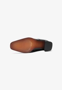 Scarpa nera con suola in gomma testurizzata, caratterizzata da una tomaia in pelle liscia. Il tacco è quadrato e di altezza moderata.