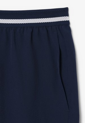 Pantalones azul marino con cinturilla elástica que incluye un detalle de malla a rayas azul marino y blanca y un bolsillo lateral sobre un fondo blanco.