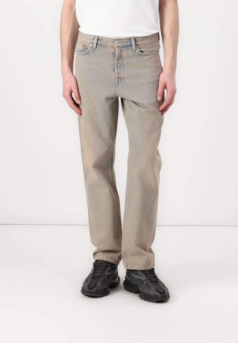 Jeans dritti beige chiaro con un classico design a cinque tasche, dettagli cuciti e una texture leggermente sbiadita. Abbinati a sneakers nere.