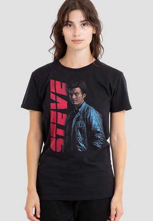 Black cotton t-shirt with short sleeves featuring a graphic print of a man in a blue jacket and the name "STEVE" in red block letters.