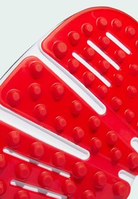 Czerwona gumowa podeszwa z wyraźnymi, okrągłymi wzorami i białymi liniami akcentującymi, prezentująca teksturowaną powierzchnię zaprojektowaną dla lepszej przyczepności i chwytu.