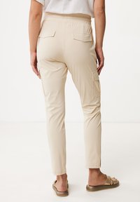 Beiga cargobyxor med elastisk midje, två bakfickor och sidofickor. Slät textur och avsmalnande ben, bärs med bruna sandaler.