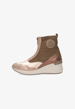 Botín deportivo de caña alta en beige y marrón con cremallera frontal, tobillo acolchado, suela blanca gruesa y parche circular de logo cerca del tobillo.