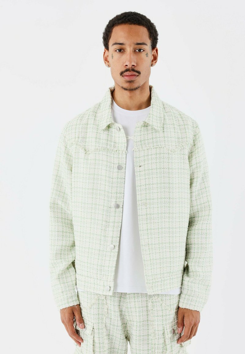 Veste en denim à motif vert clair avec un devant à boutons, deux poches poitrine et un col, portée sur une chemise blanche.